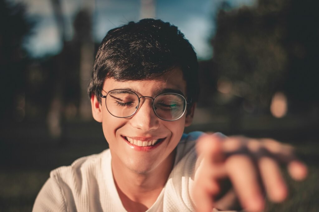 pexels-photo-2829792-2829792 A joyful young man wearing glasses smiles in an outdoor setting with blurred background.